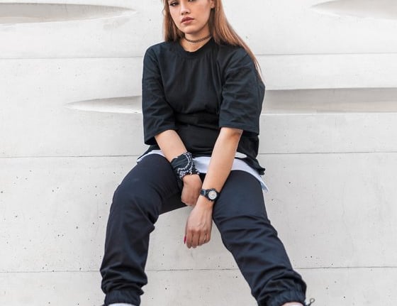 woman in black long sleeve shirt and blue denim jeans sitting on white concrete wall