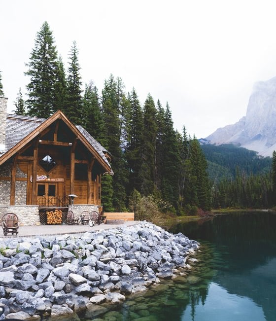 brown wooden house near lake surrounded by green trees during daytime