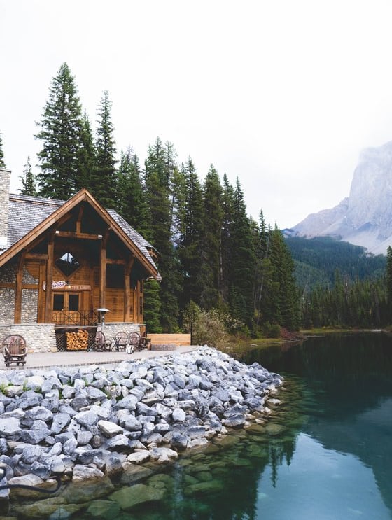 brown wooden house near lake surrounded by green trees during daytime