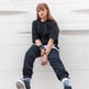 woman in black long sleeve shirt and blue denim jeans sitting on white concrete wall