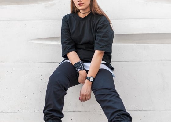 woman in black long sleeve shirt and blue denim jeans sitting on white concrete wall