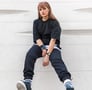 woman in black long sleeve shirt and blue denim jeans sitting on white concrete wall