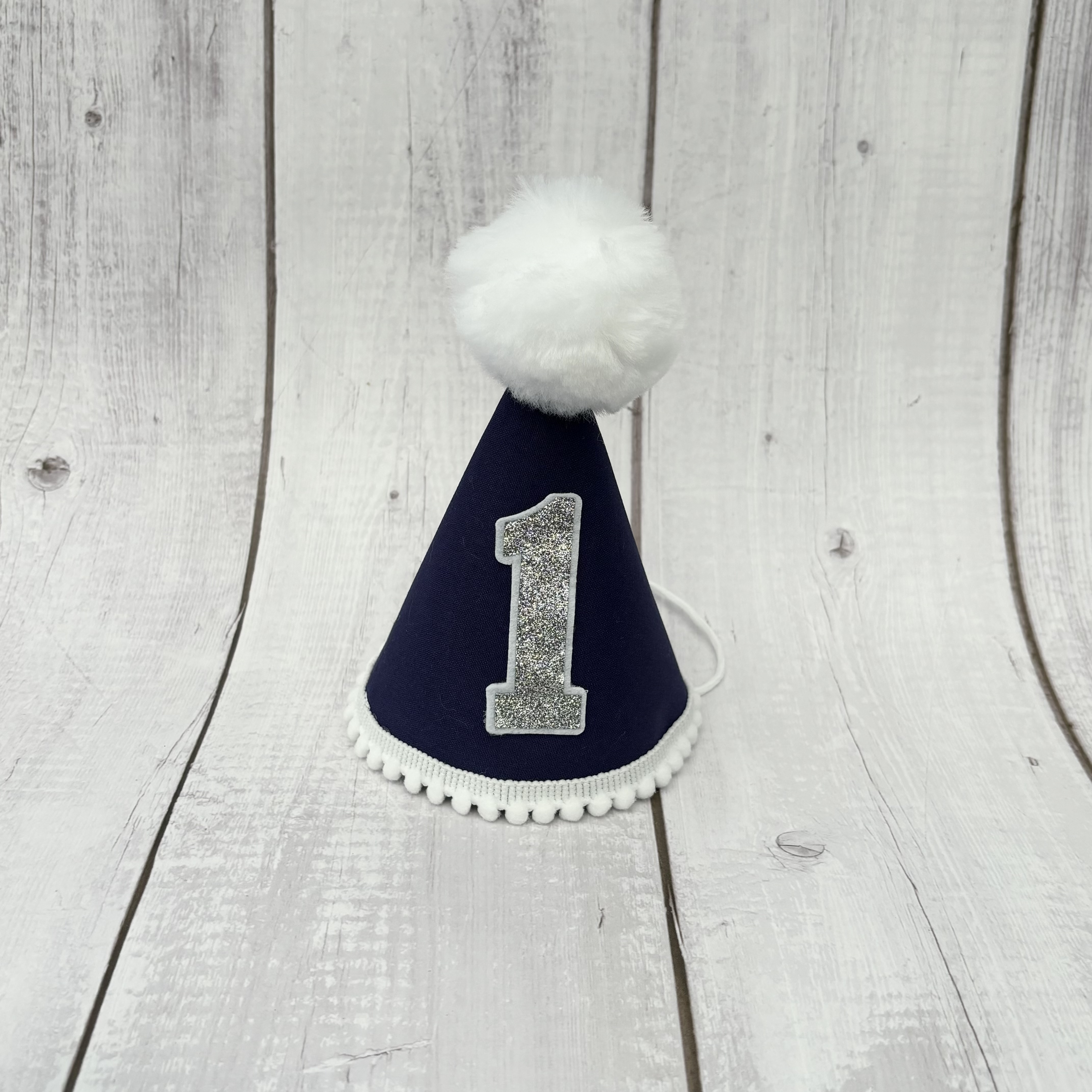 Navy blue child's party hat with white trims and pom pom