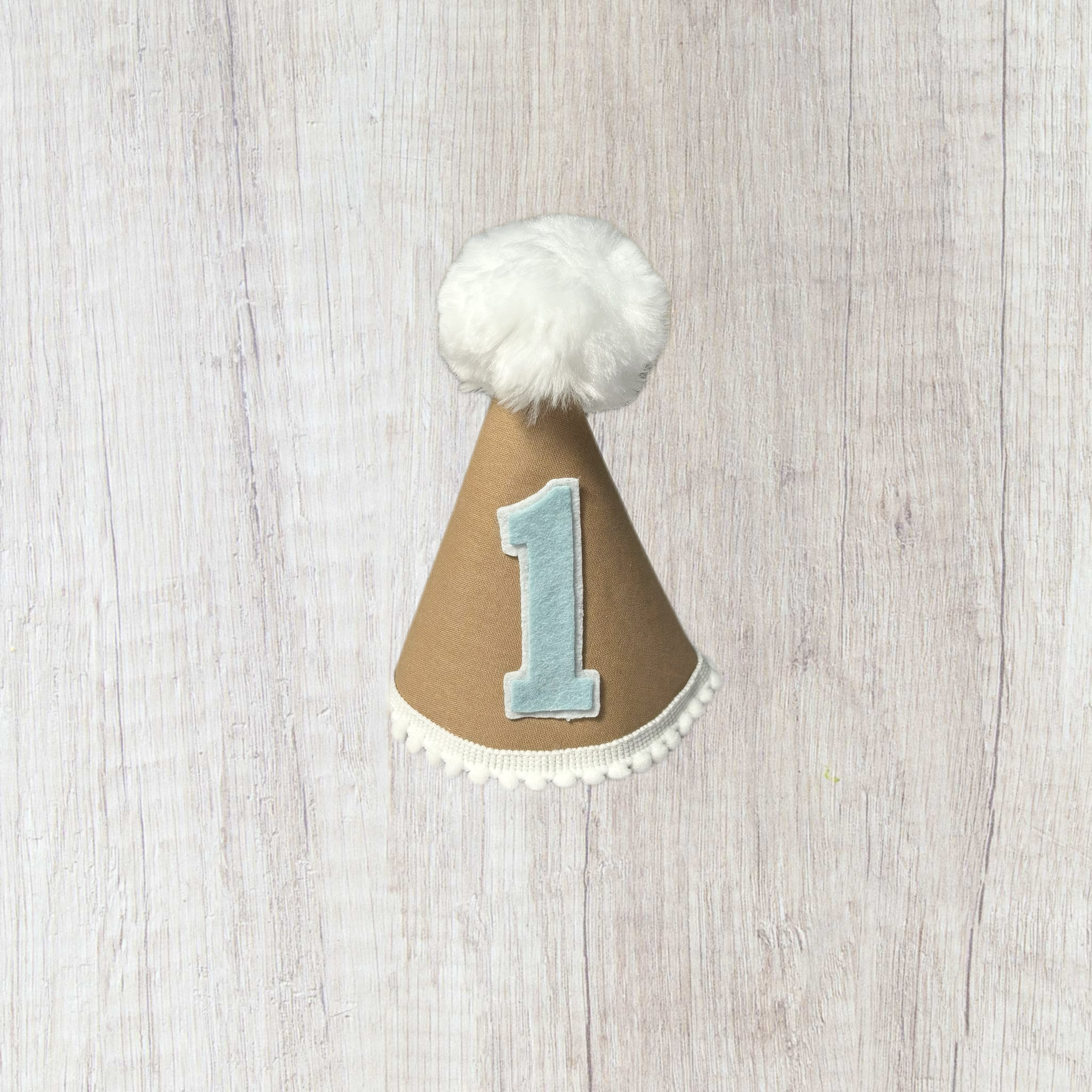 Tan child's party hat with white trims and pom pom