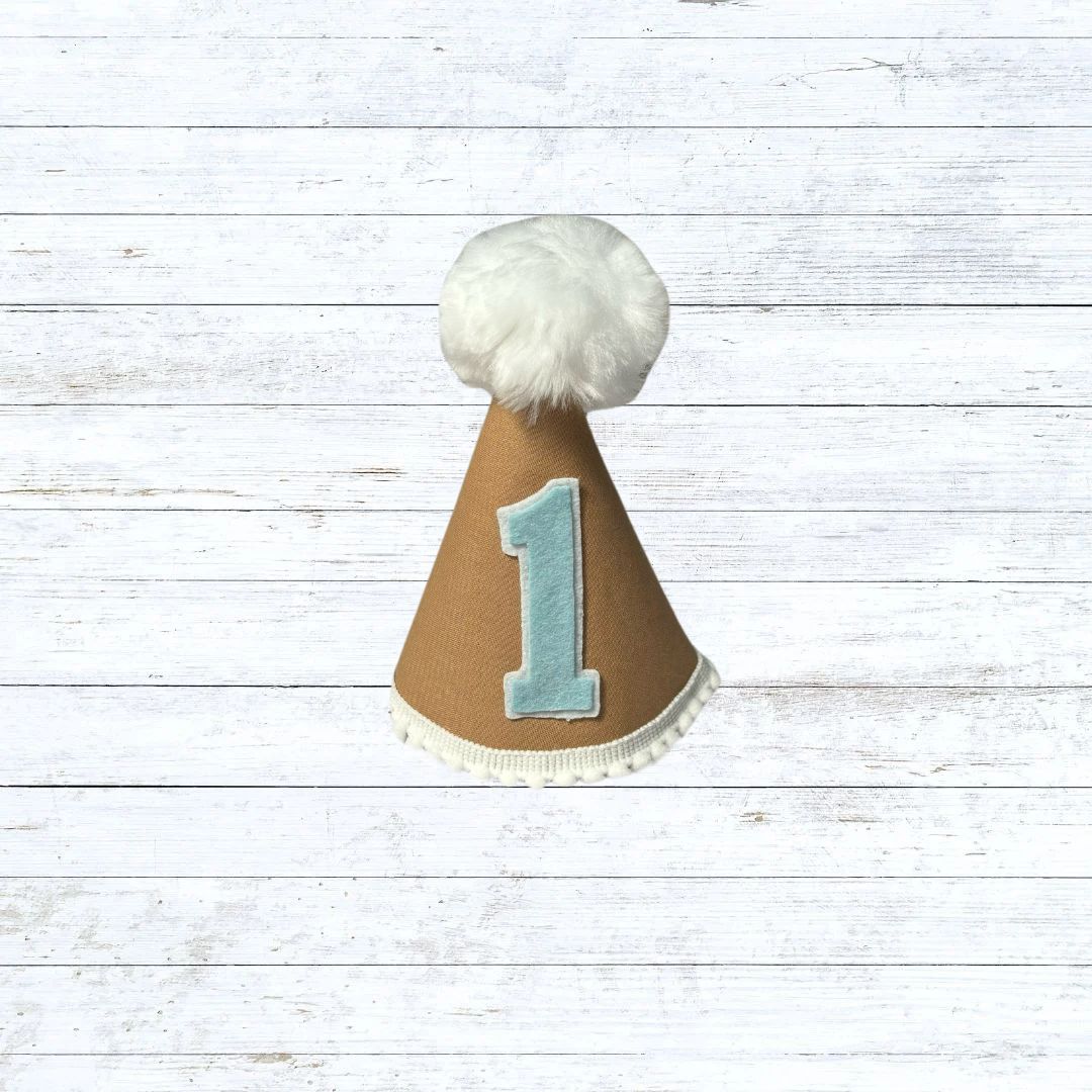Tan child's party hat with white trims and pom pom
