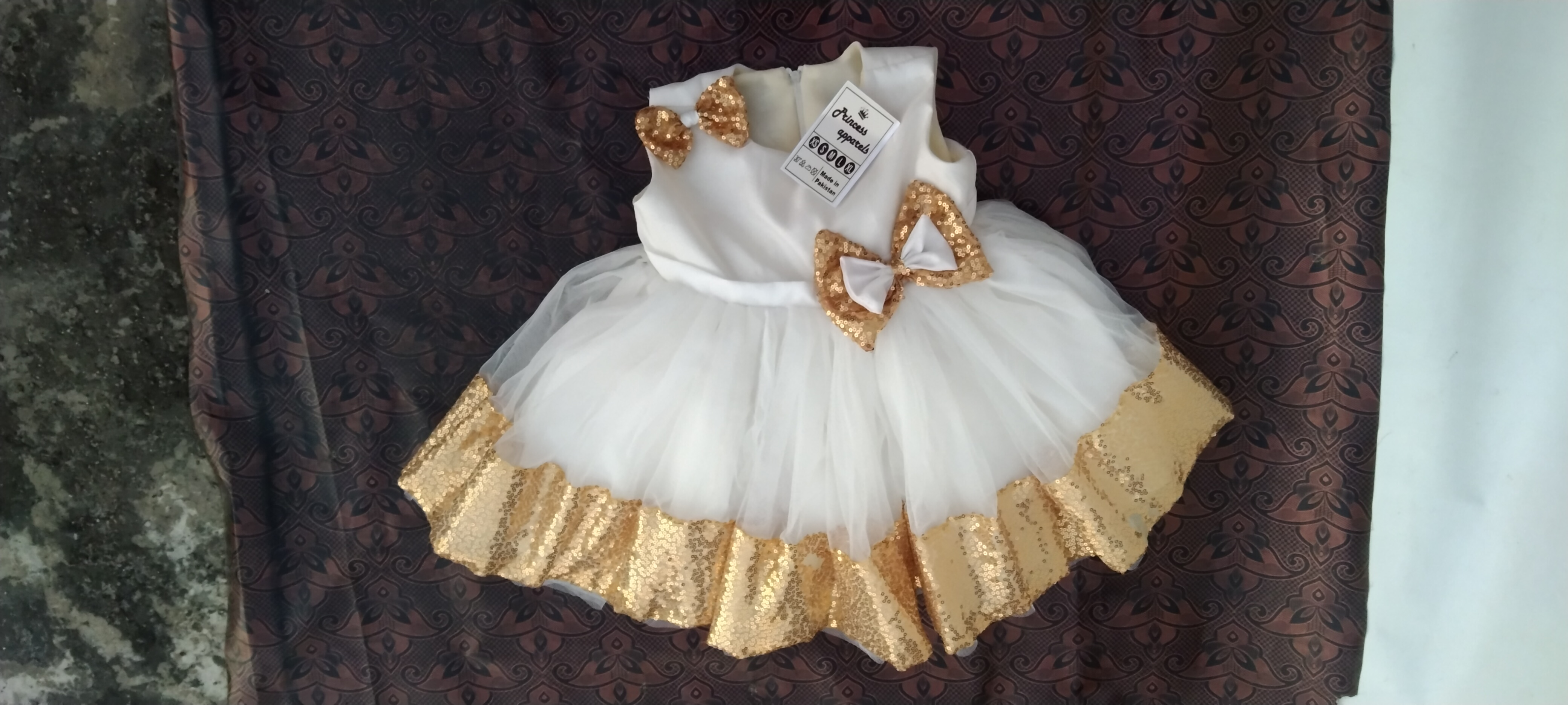 Golden Hour Glam,  handcrafted party dress for baby girls features white silk and net, gold sequins, delicate bows, and a multi-layered skirt for graceful movement.