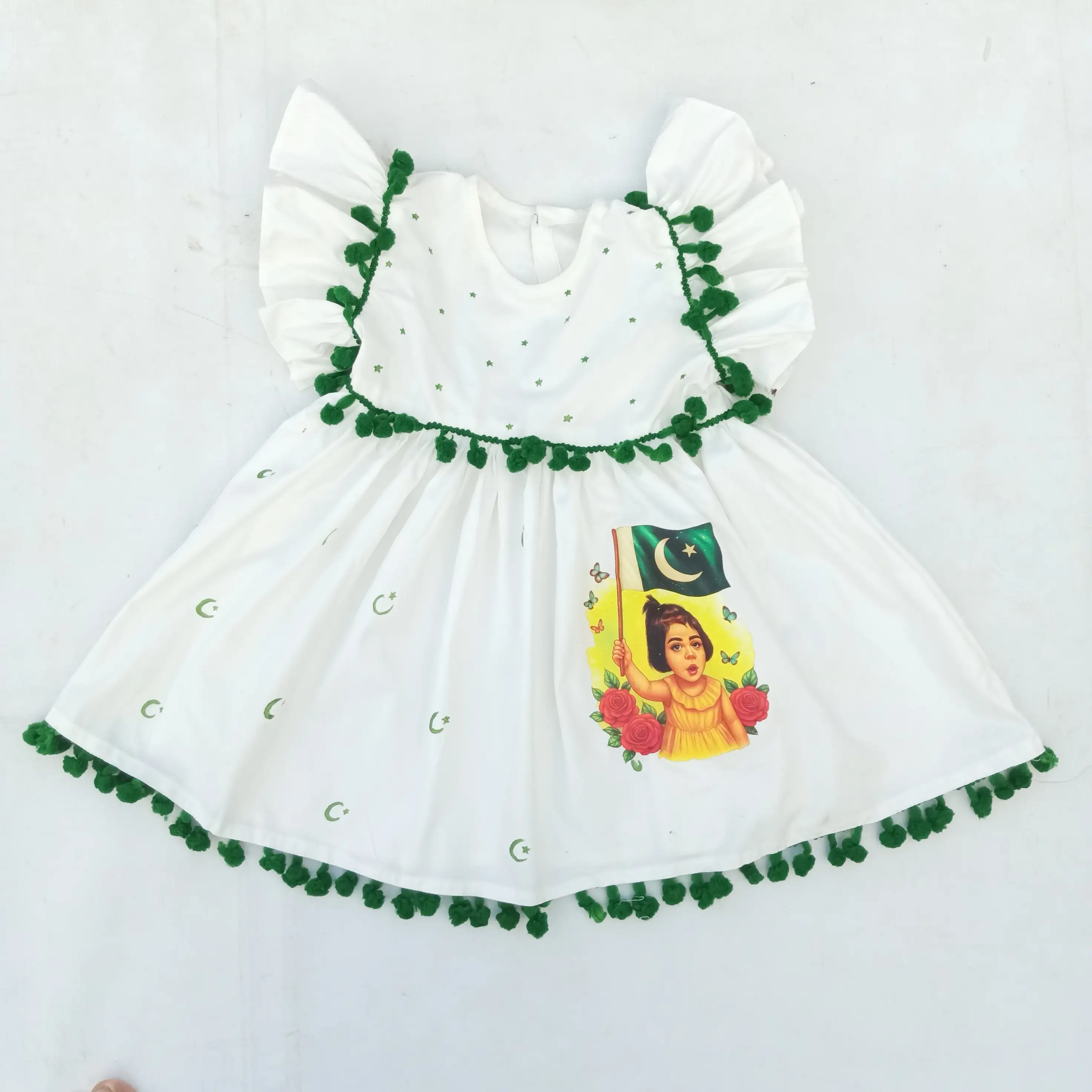 Starry Blossom Frock Patriotic Elegance for Little Hearts "A young girl in a white Pakistani Independence Day dress, holding a white flower in a garden."