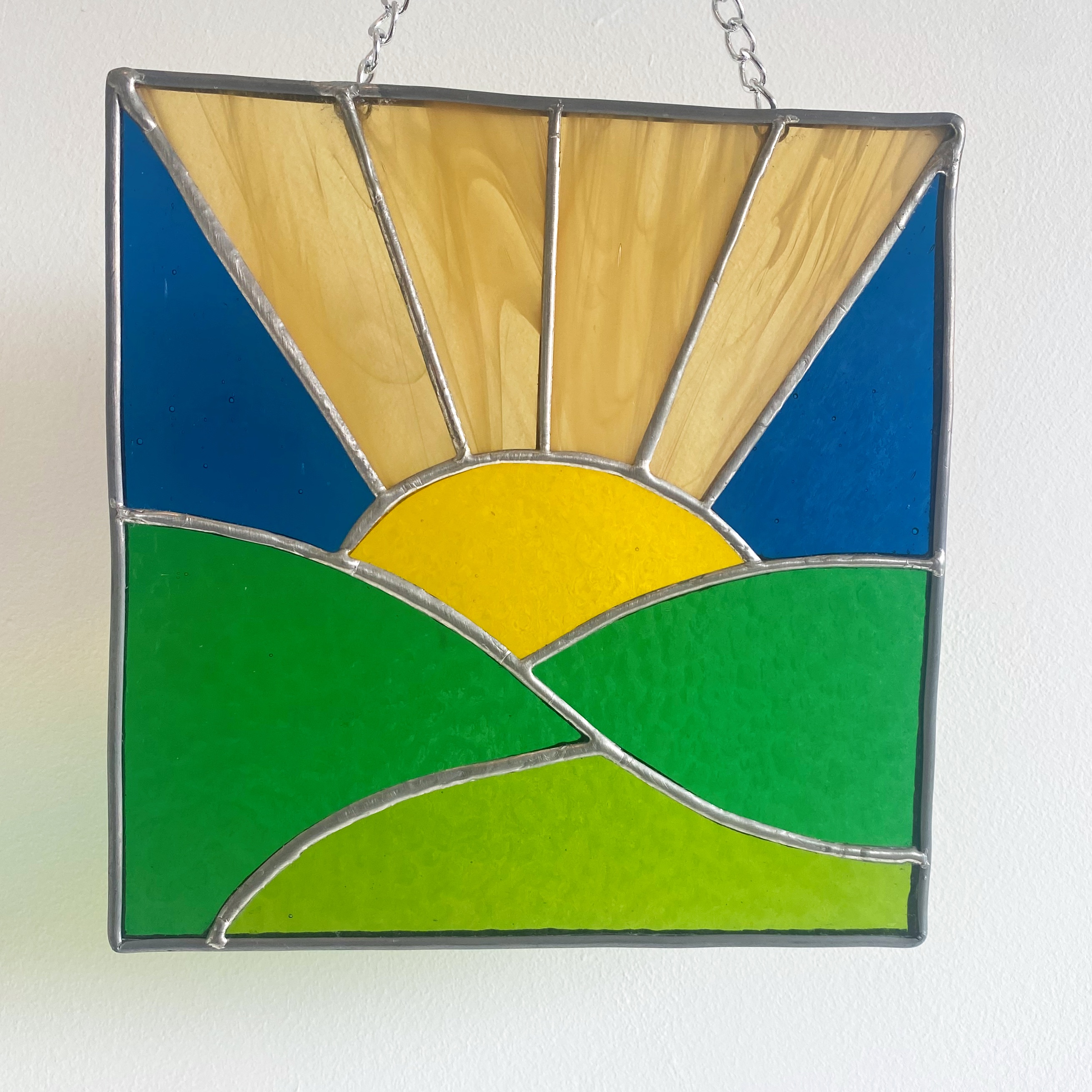 Stained glass sunrise over green fields.