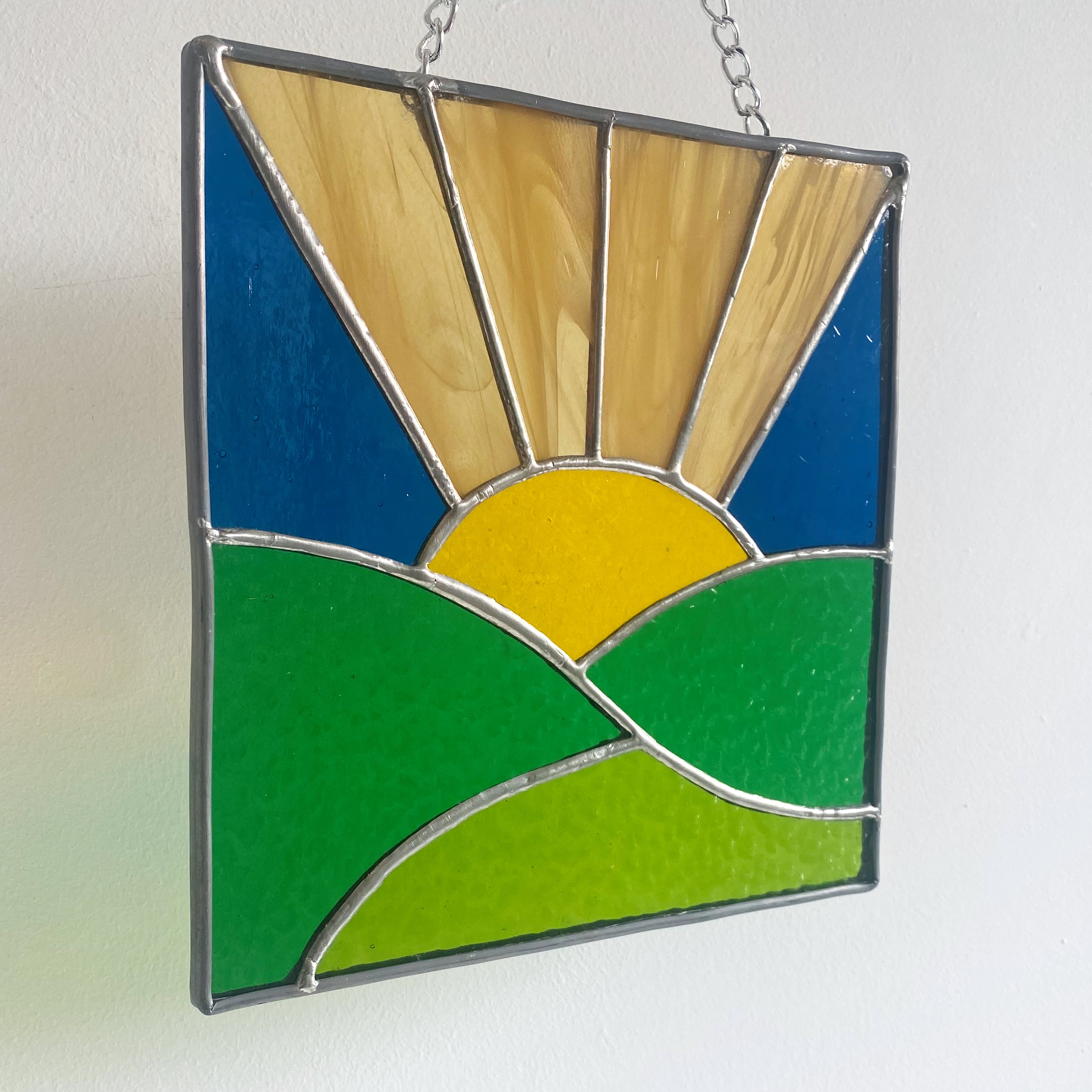 Stained glass sunrise over green fields.