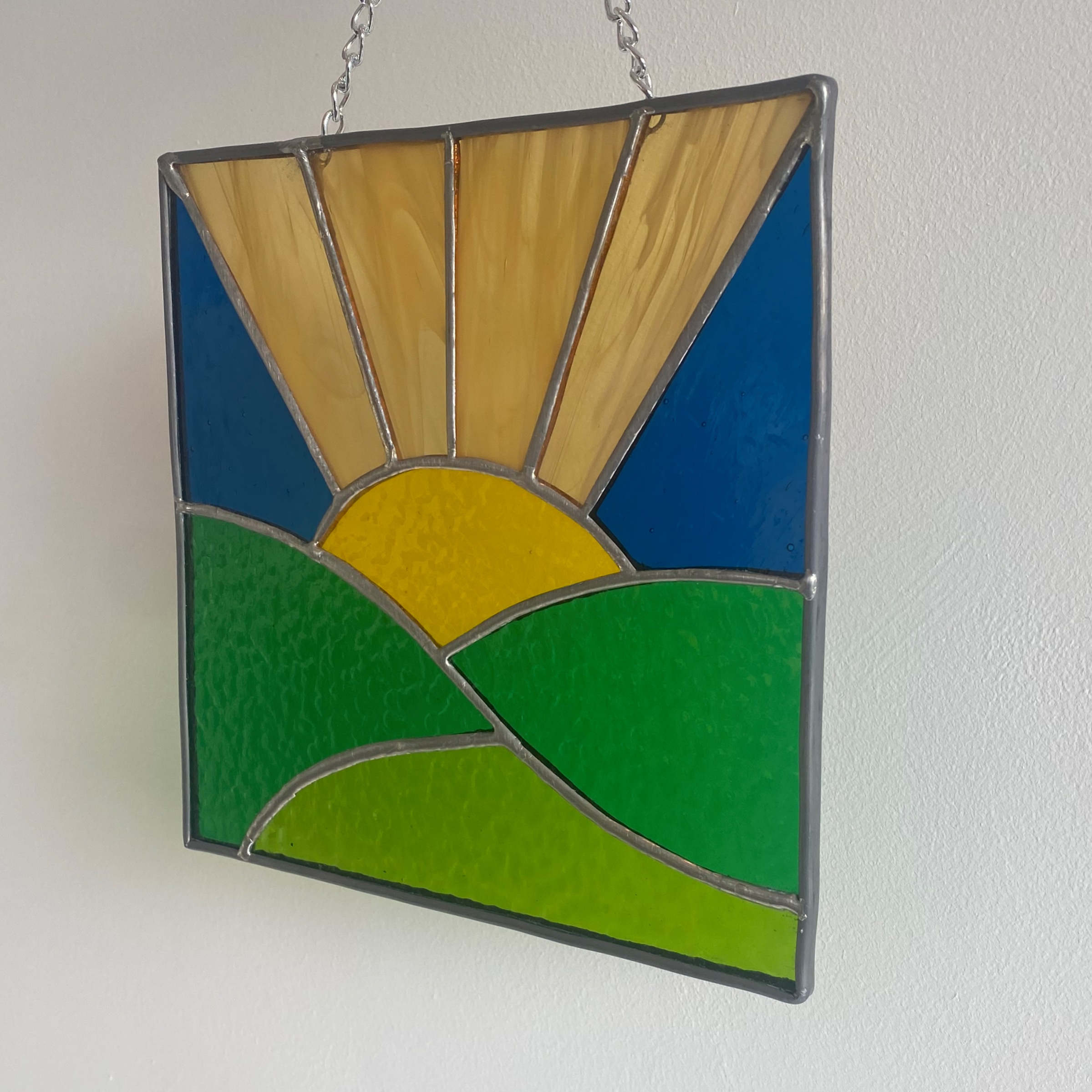 Stained glass sunrise over green fields.