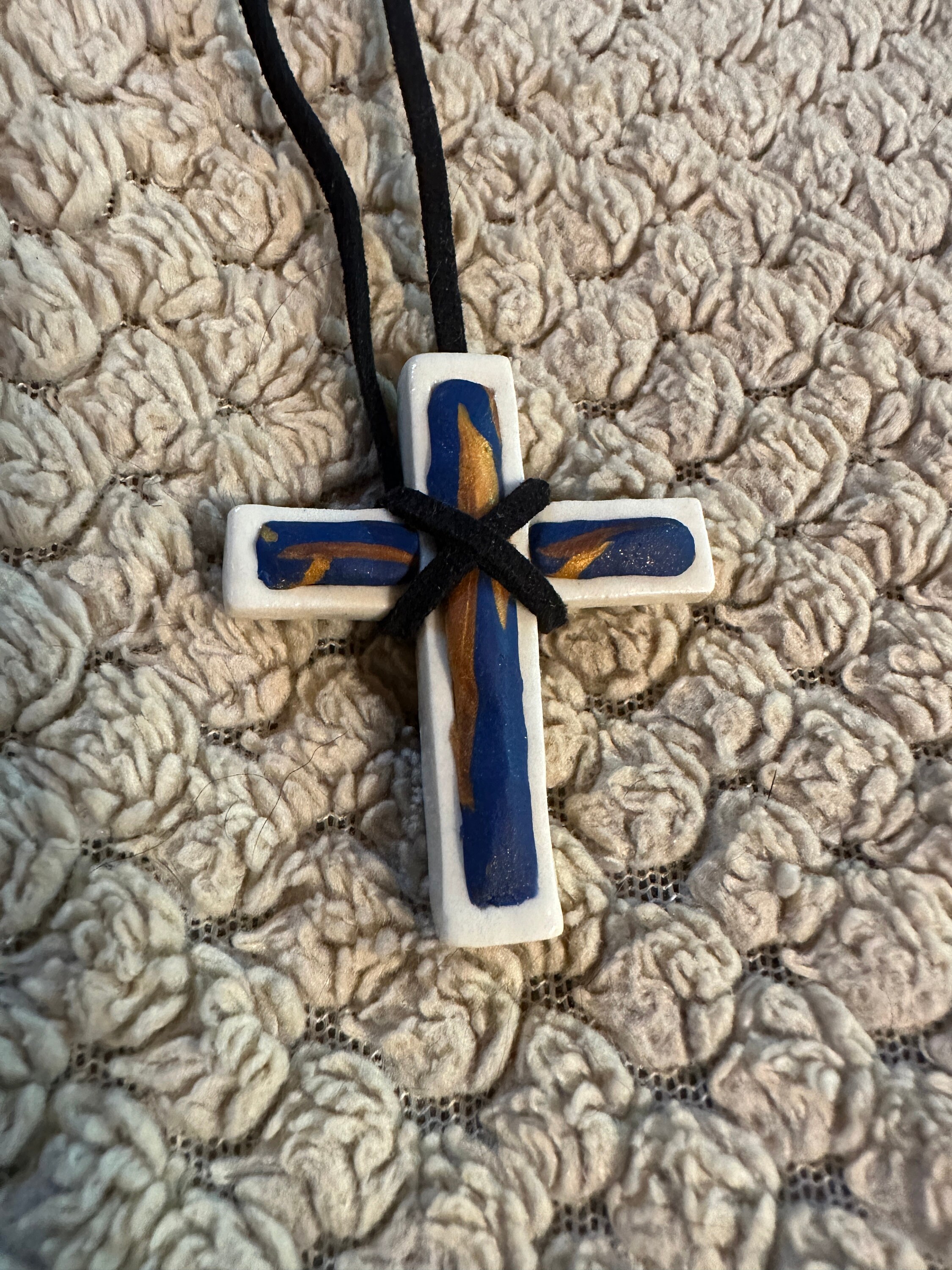 White hand made porcelain Christian cross with copper and royal blue polymer design fill on black suede cord with barrel clasp