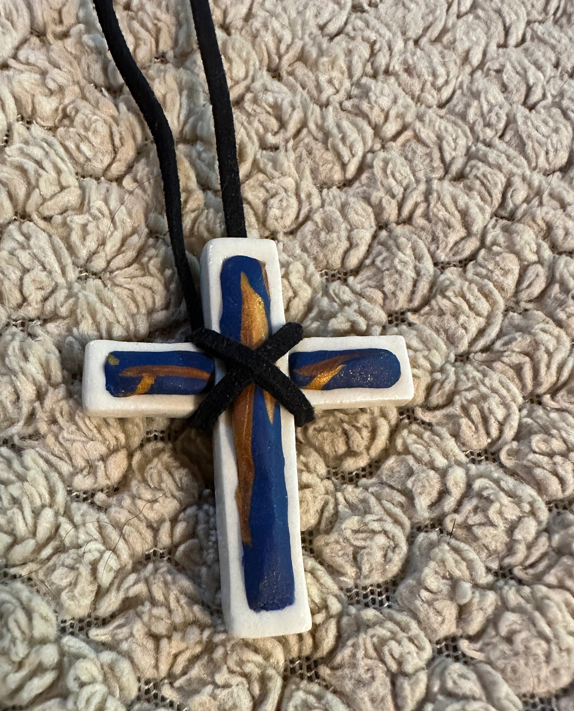 White hand made porcelain Christian cross with copper and royal blue polymer design fill on black suede cord with barrel clasp