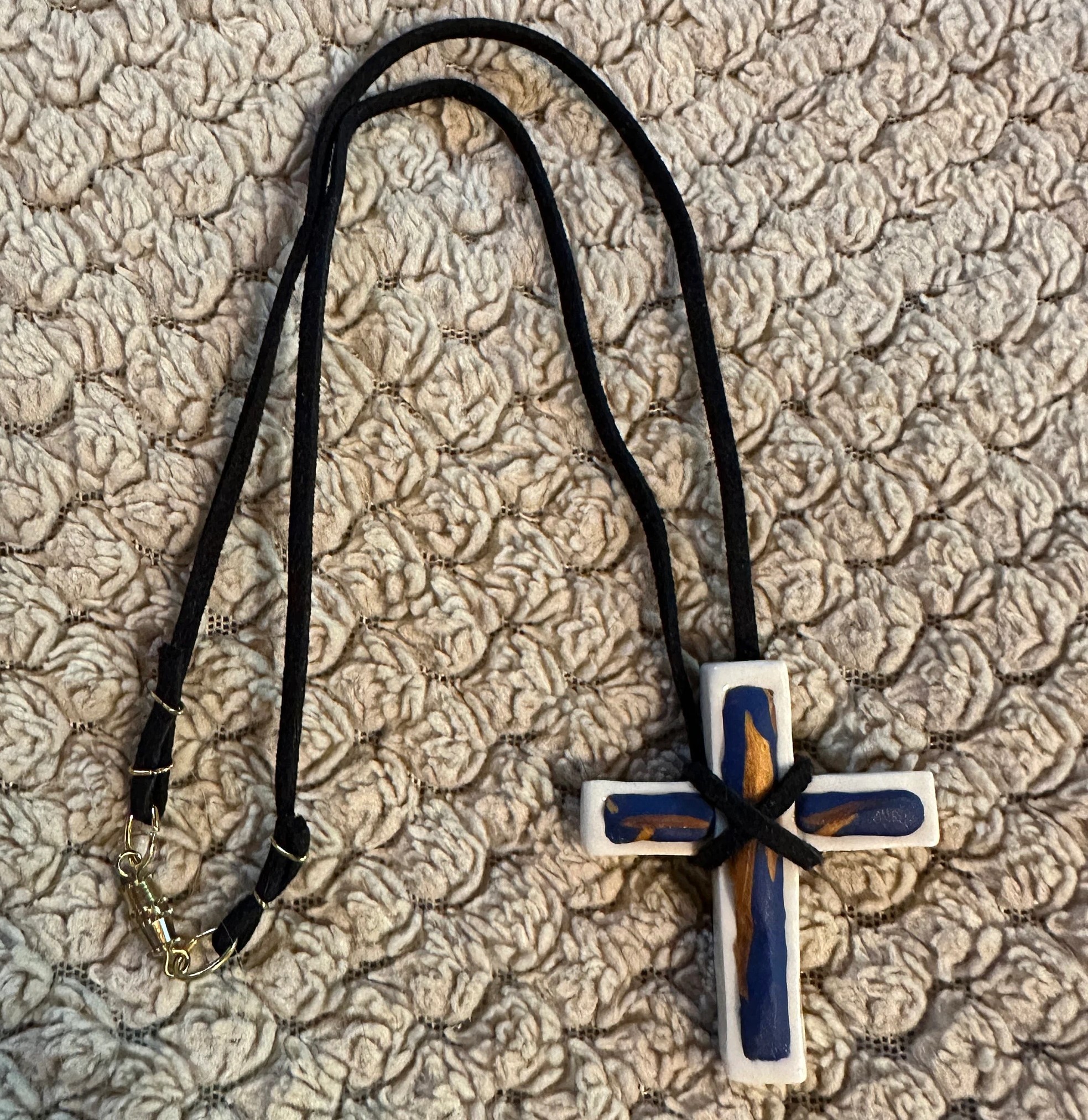 White hand made porcelain Christian cross with copper and royal blue polymer design fill on black suede cord with barrel clasp