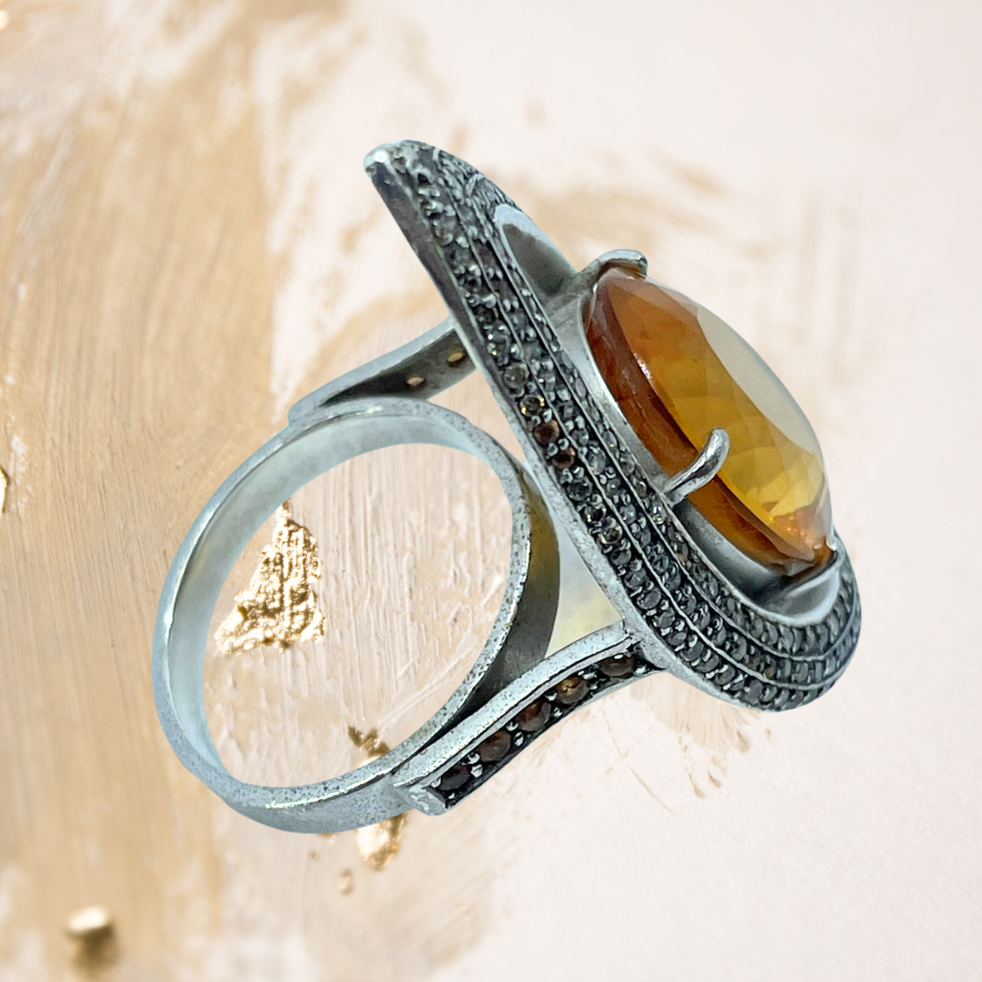 Este anel em prata revela o brilho intenso de uma pedra preciosa oval em tom laranja vibrante.