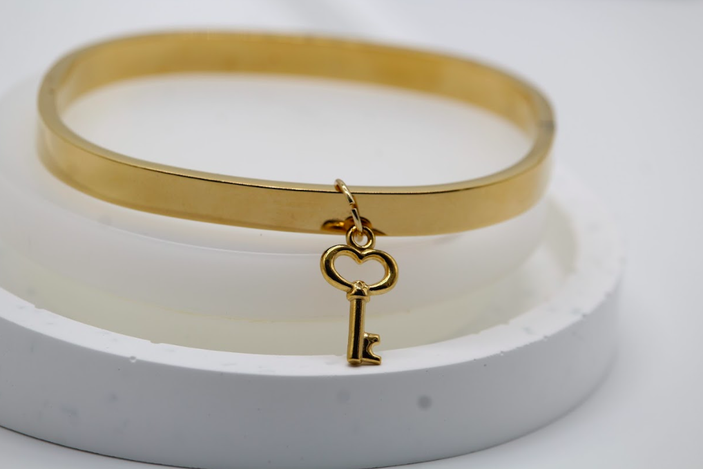 Pulsera tipo brazalete dorada con dije de llave