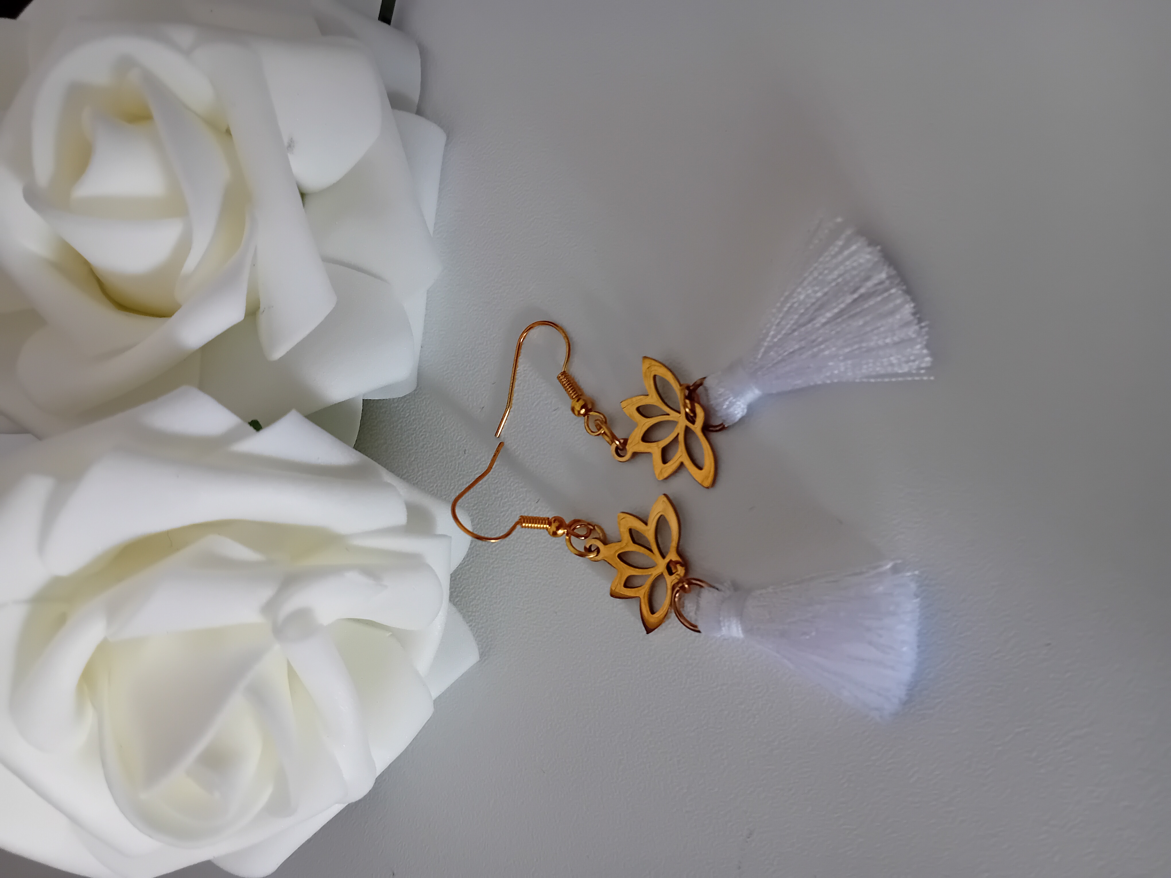 Bijou en chaîne dorée avec pendentif fleur de lotus et boucle d'oreille avec son pompon blanc.