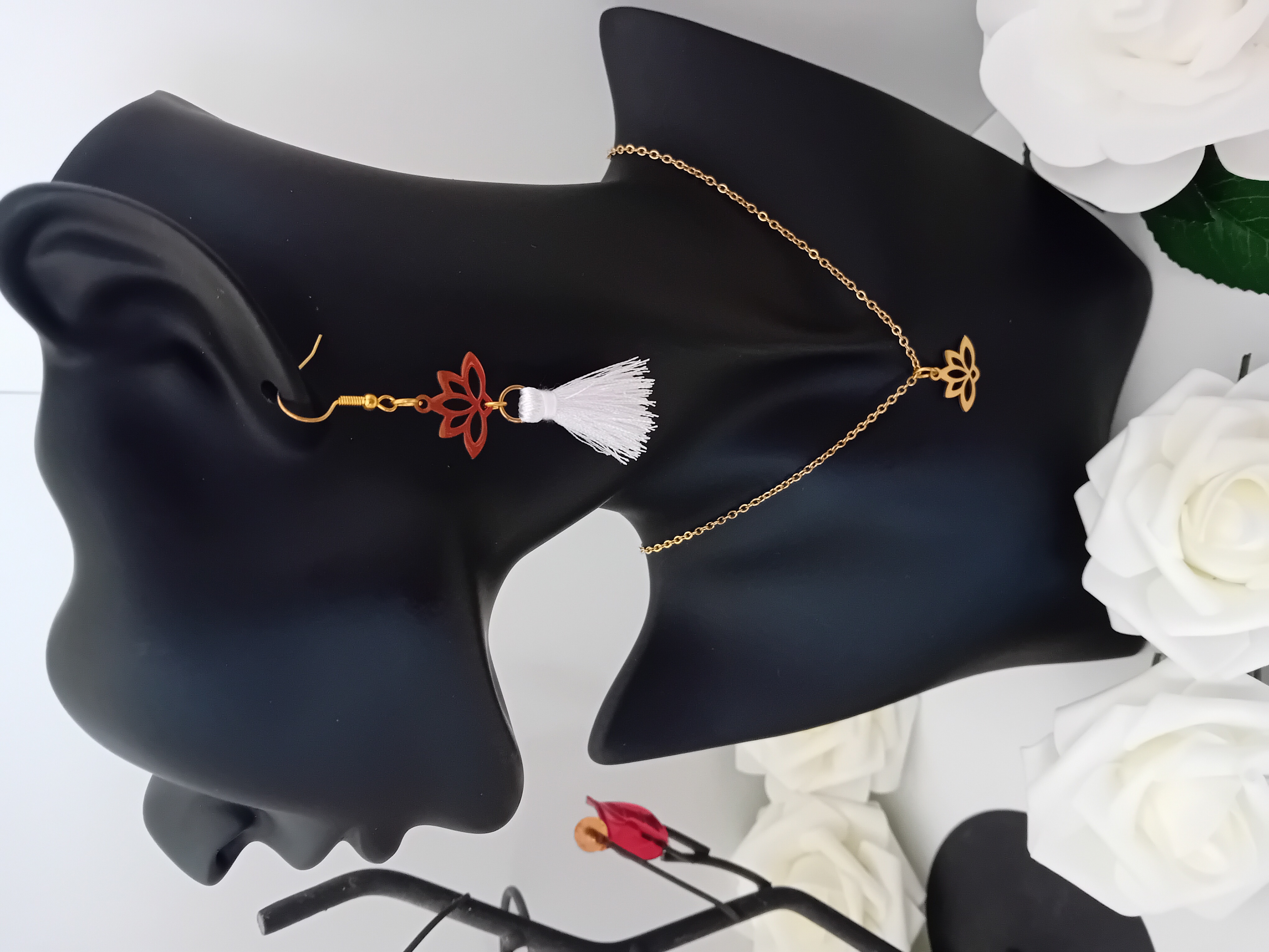 Bijou en chaîne dorée avec pendentif fleur de lotus et boucle d'oreille avec son pompon blanc.