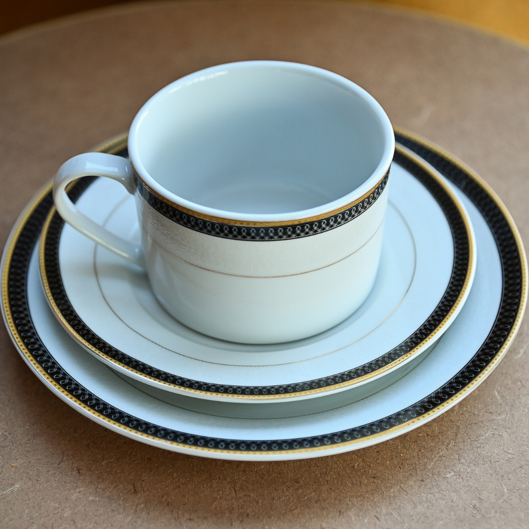 Conjunto com xícara, pires e prato em porcelana branca com borda preta e filetes dourados