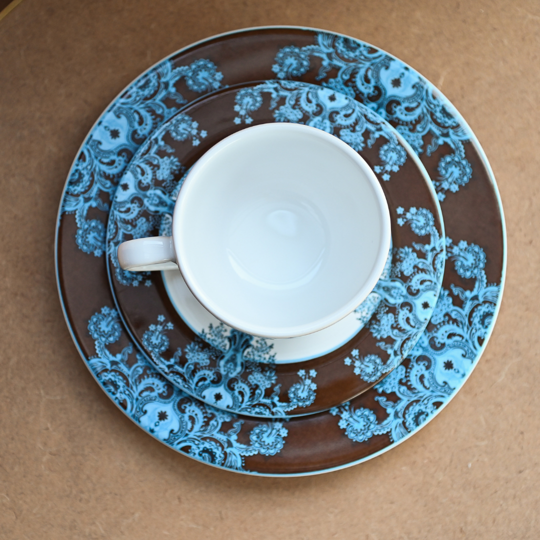 Conjunto com xícara, pires e prato de sobremesa em porcelana com estampa floral azul e fundo marrom