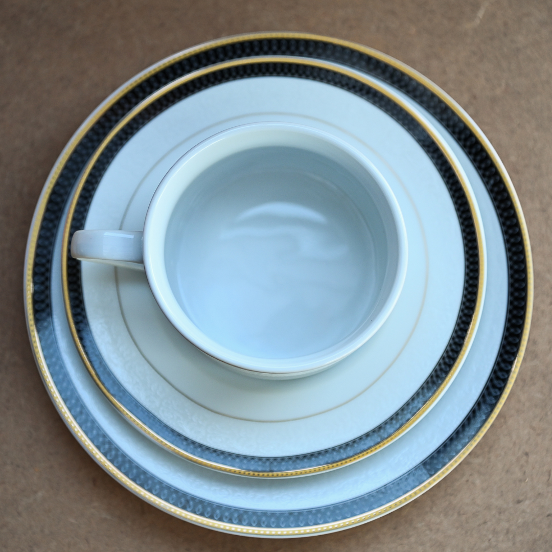 Conjunto com xícara, pires e prato em porcelana branca com borda preta e filetes dourados