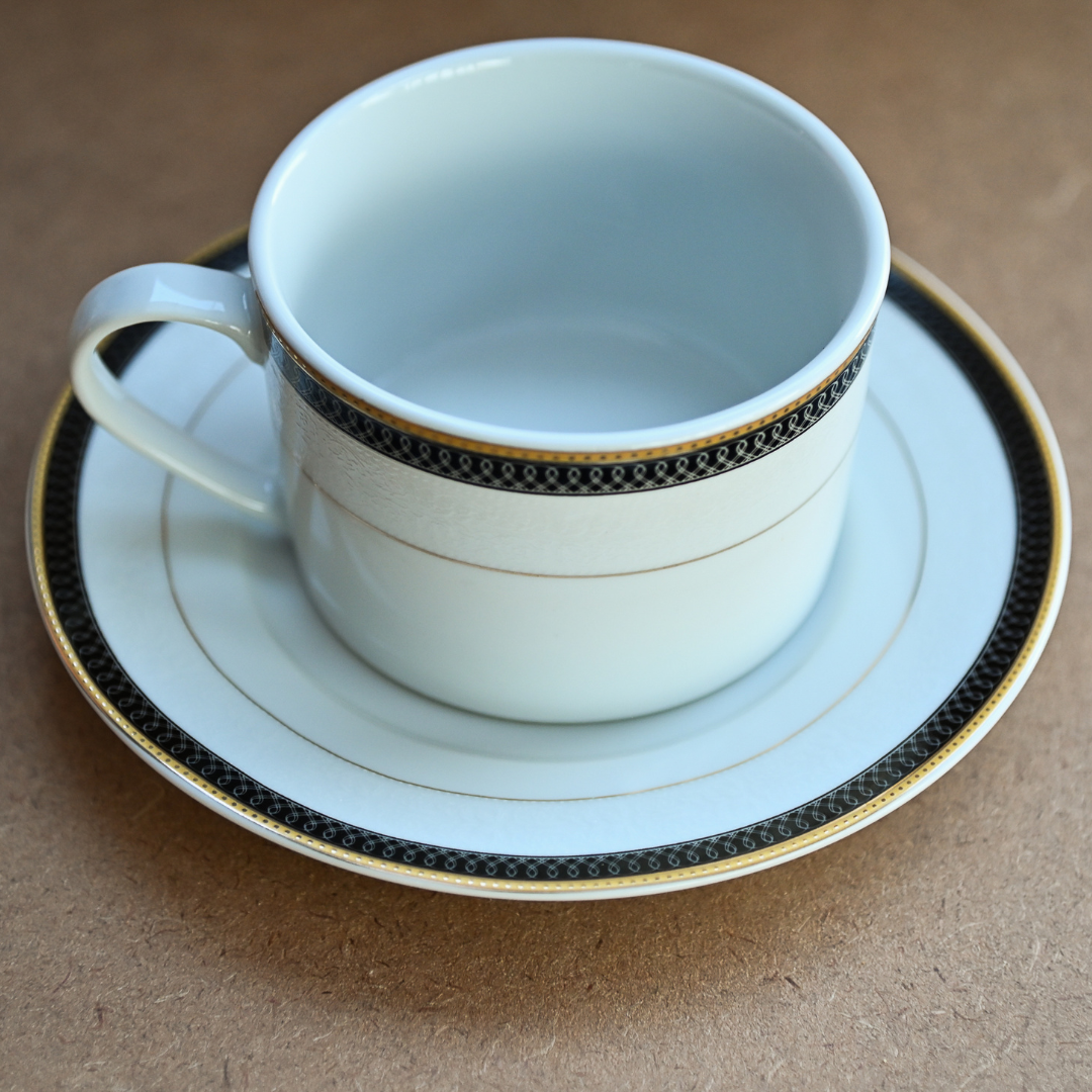 Xícara com pires em porcelana branca com borda preta e filetes dourados