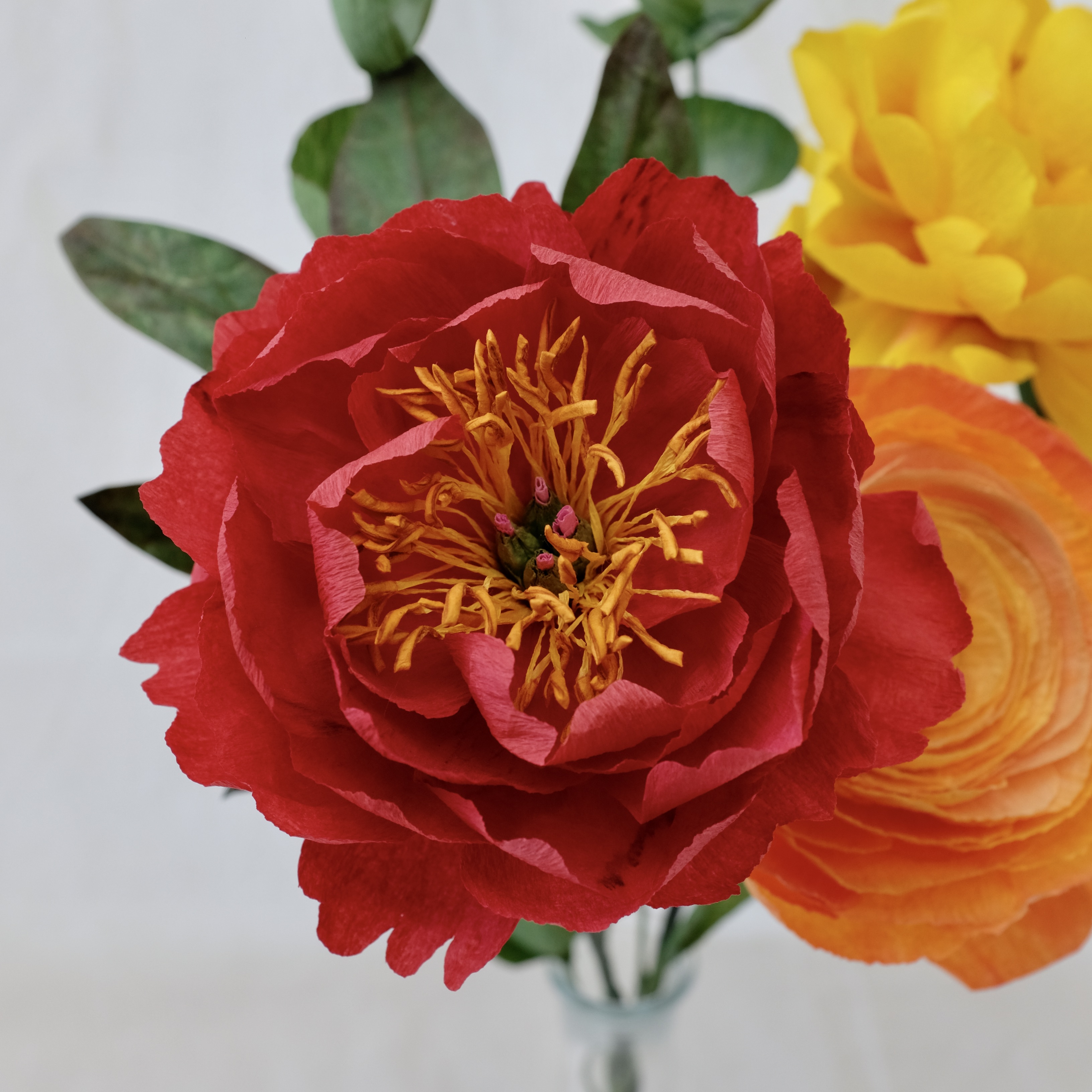 Bouquet de fleurs en papier : pivoine rouge, pivoine jaune,  renoncule orange et trois brins d'eucalyptus