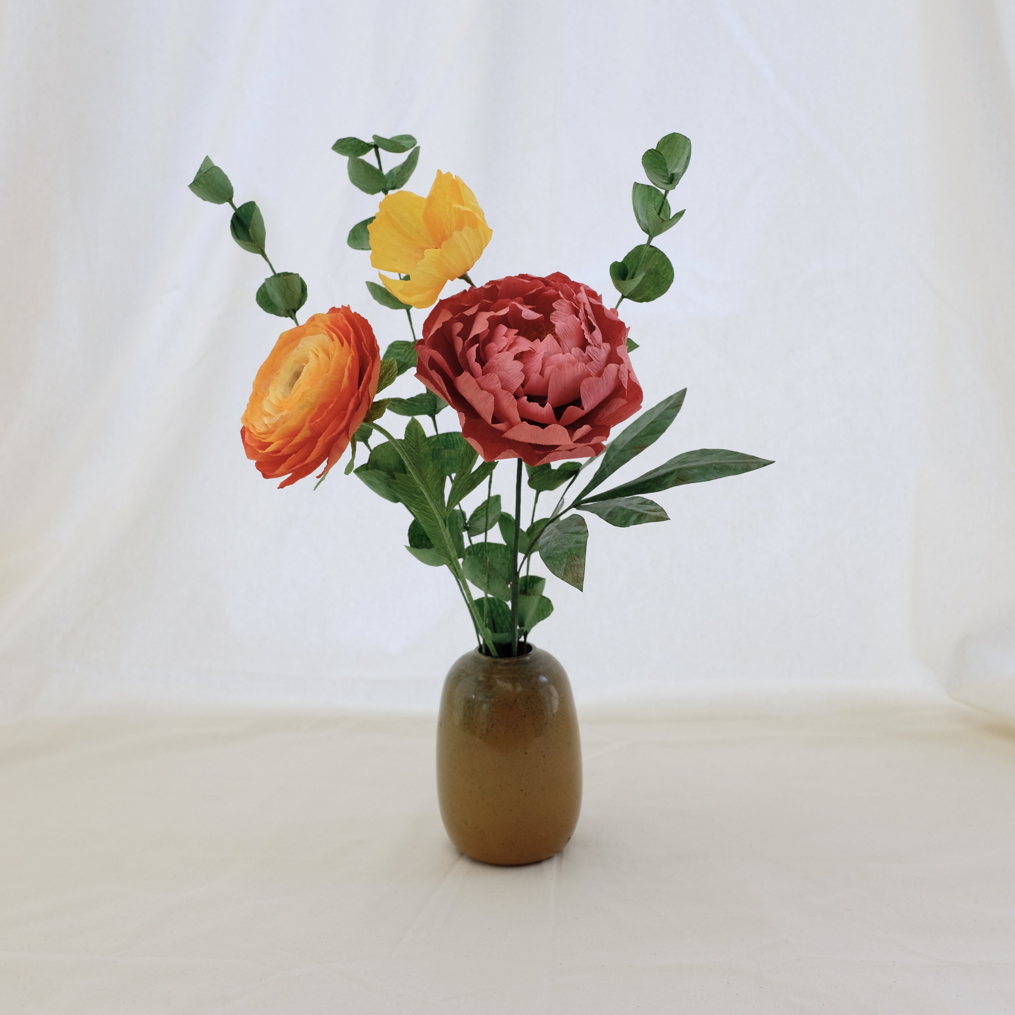 Bouquet de fleurs en papier : pivoine rose, renoncule orange, cosmos jaune, et trois brins d'eucalyptus