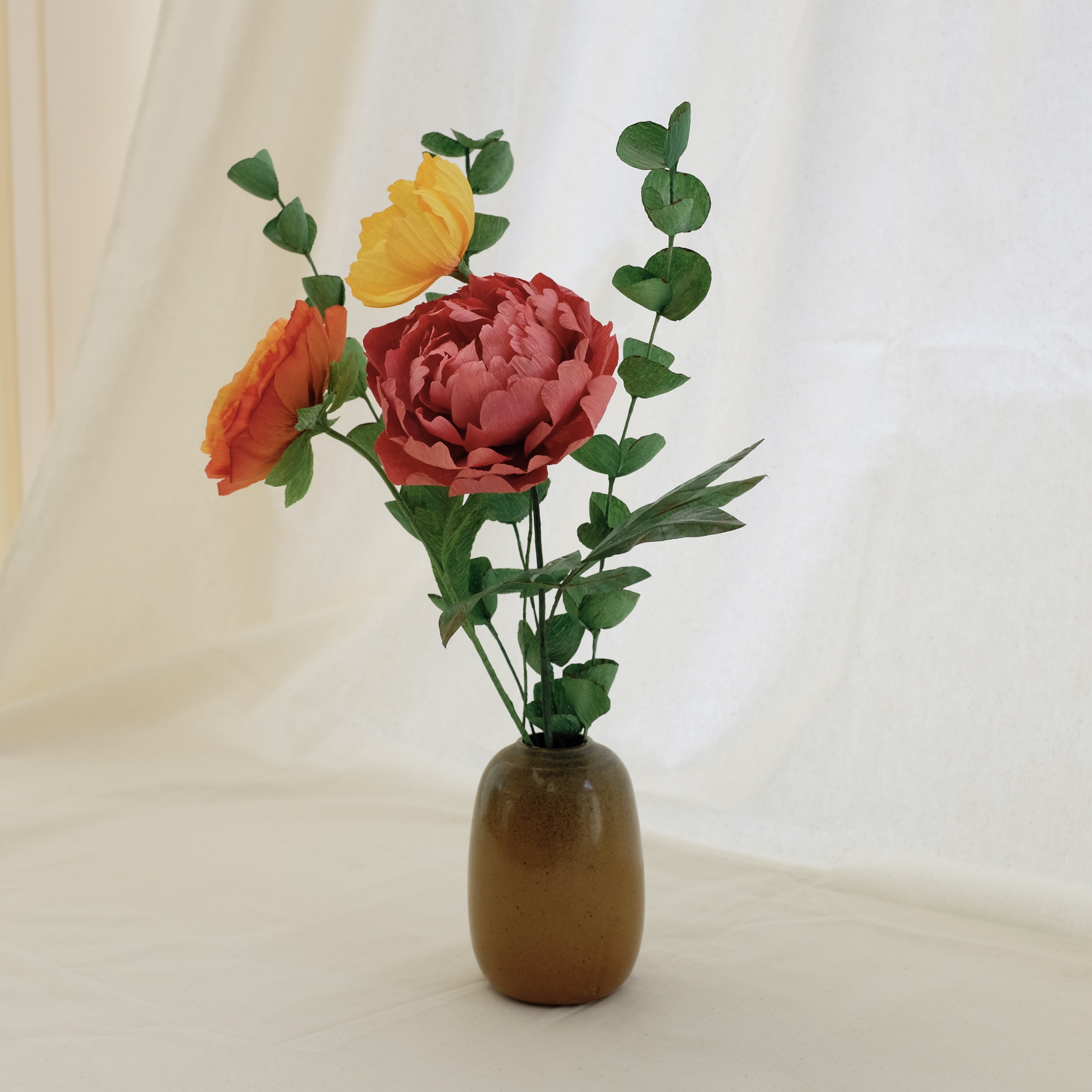 Bouquet de fleurs en papier : pivoine rose, renoncule orange, cosmos jaune, et trois brins d'eucalyptus