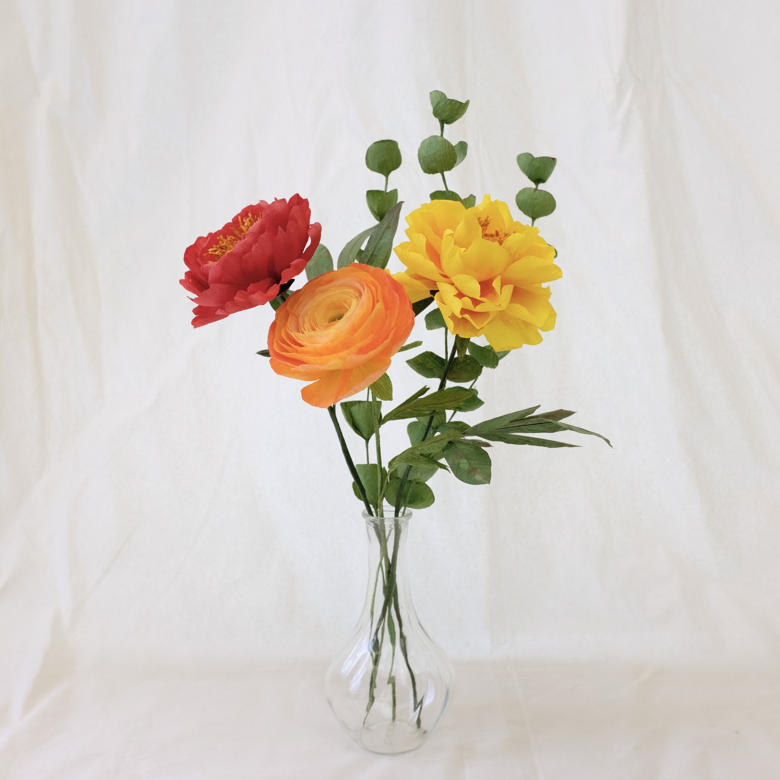 Bouquet de fleurs en papier : pivoine rouge, pivoine jaune,  renoncule orange et trois brins d'eucalyptus