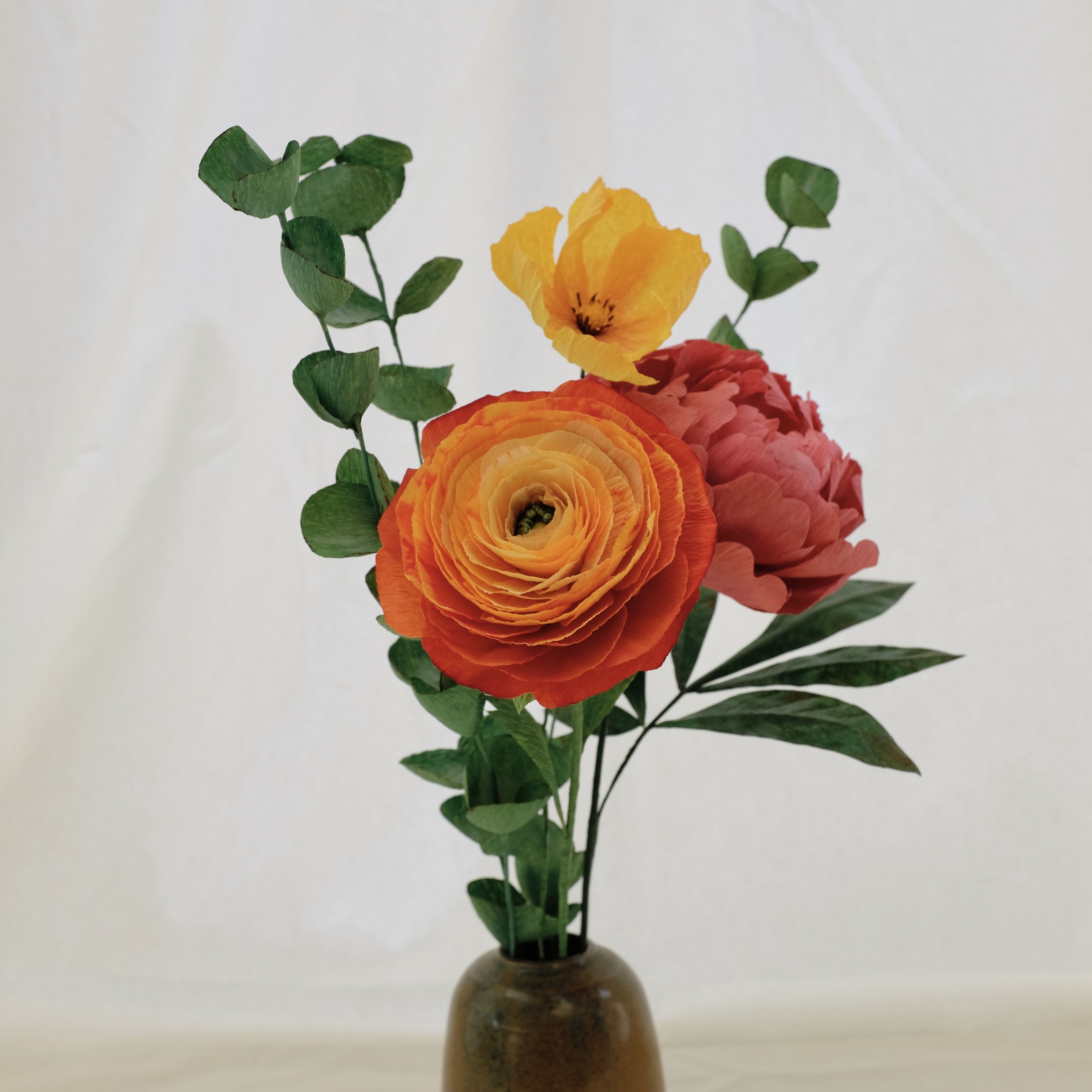 Bouquet de fleurs en papier : pivoine rose, renoncule orange, cosmos jaune, et trois brins d'eucalyptus