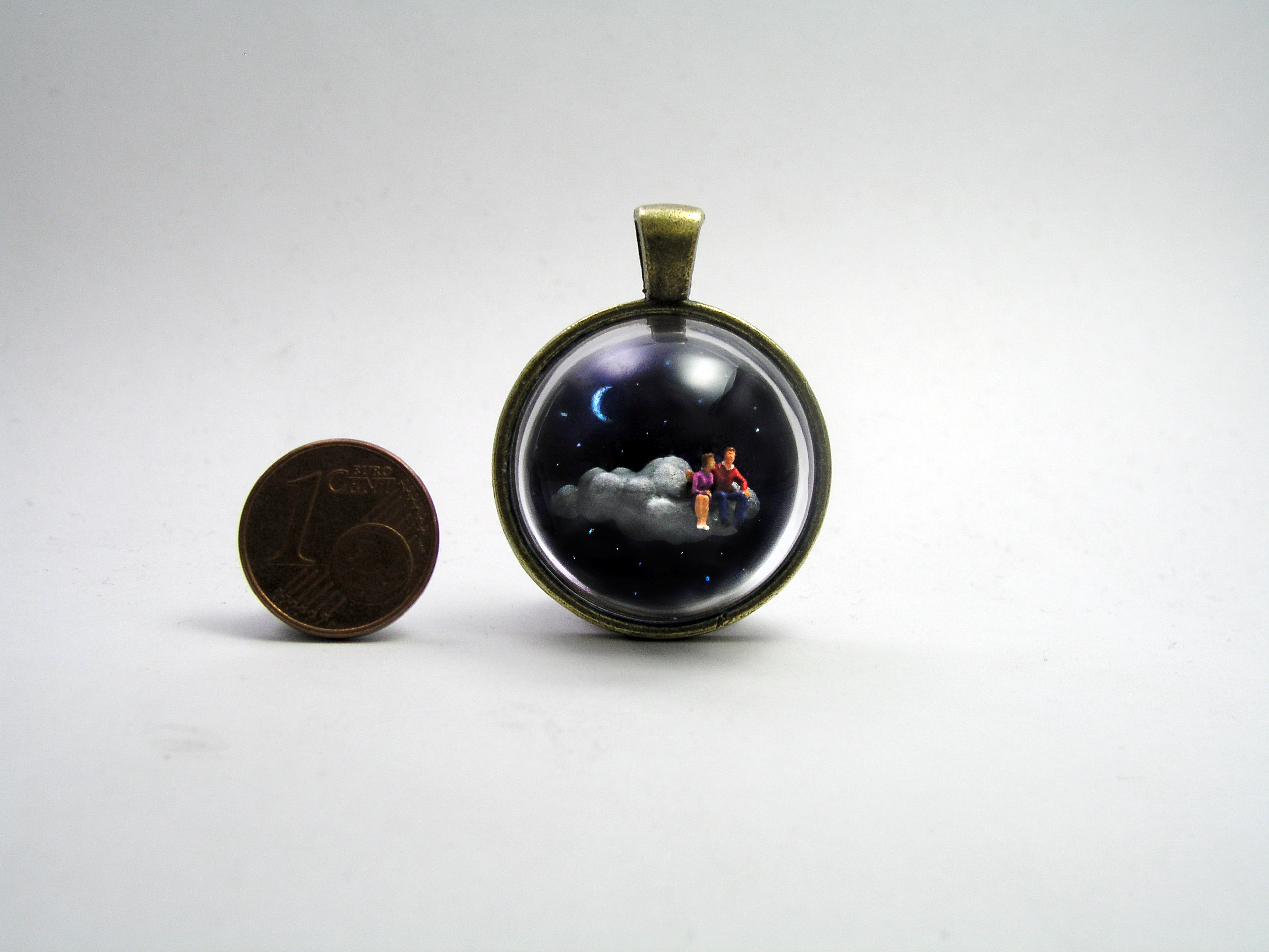 Miniature World pendant. A miniature man and woman are sitting on a cloud travelling through the night sky